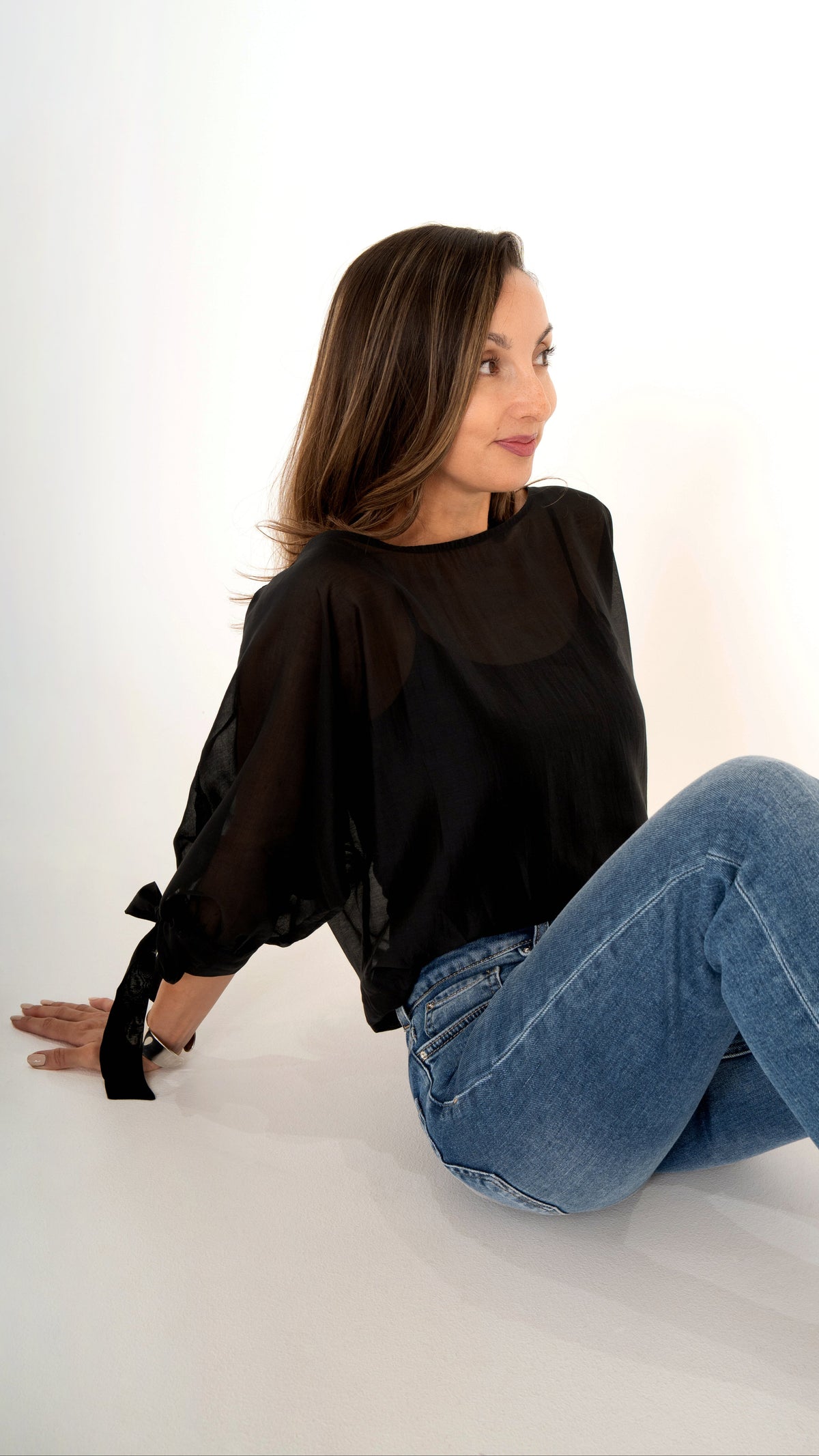 Seitenansicht sitzend Damenkleidung: blaue gerade Jeans mit schwarzer Volumen Bluse