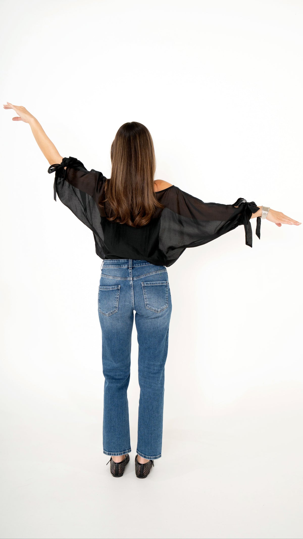 Rückansicht feminines Outfit: blaue gerade Jeans mit schwarzer weiter Chiffon Bluse mit Schleifen