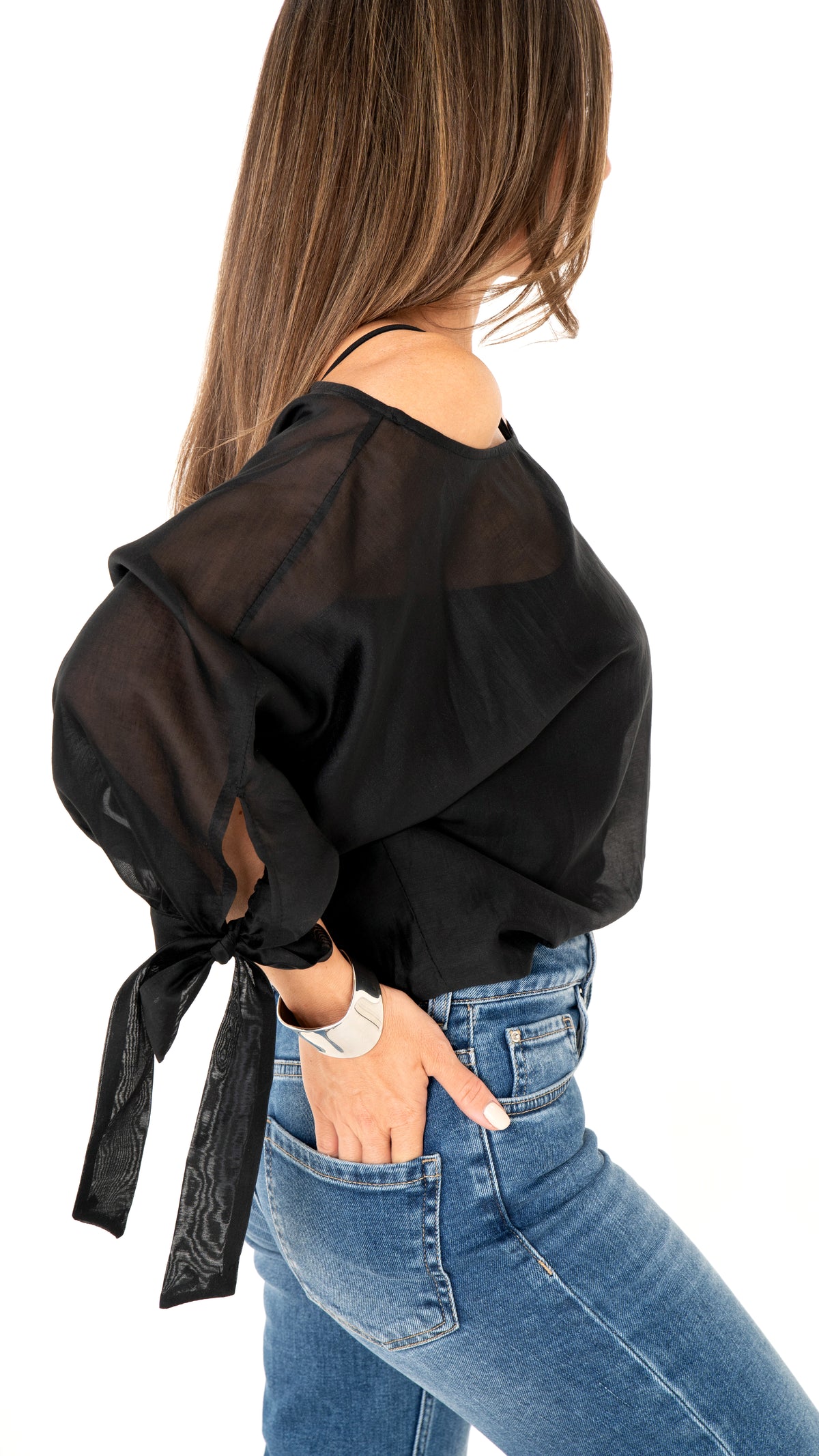 Seitenansicht Damemode: Cooles Outfit aus blauer Jeanshose und weite schwarze Bluse , halbtransparent und Schleifendetail am Ärmel