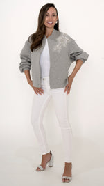 Feminine Damenmode in grau weiß: Model trägt eine coole feminine Sweat Jacke in grau mit floraler Trend Glitzer Stickerei. dazu trägt sie eine weiße Skinny Denim und ein weißes Top.