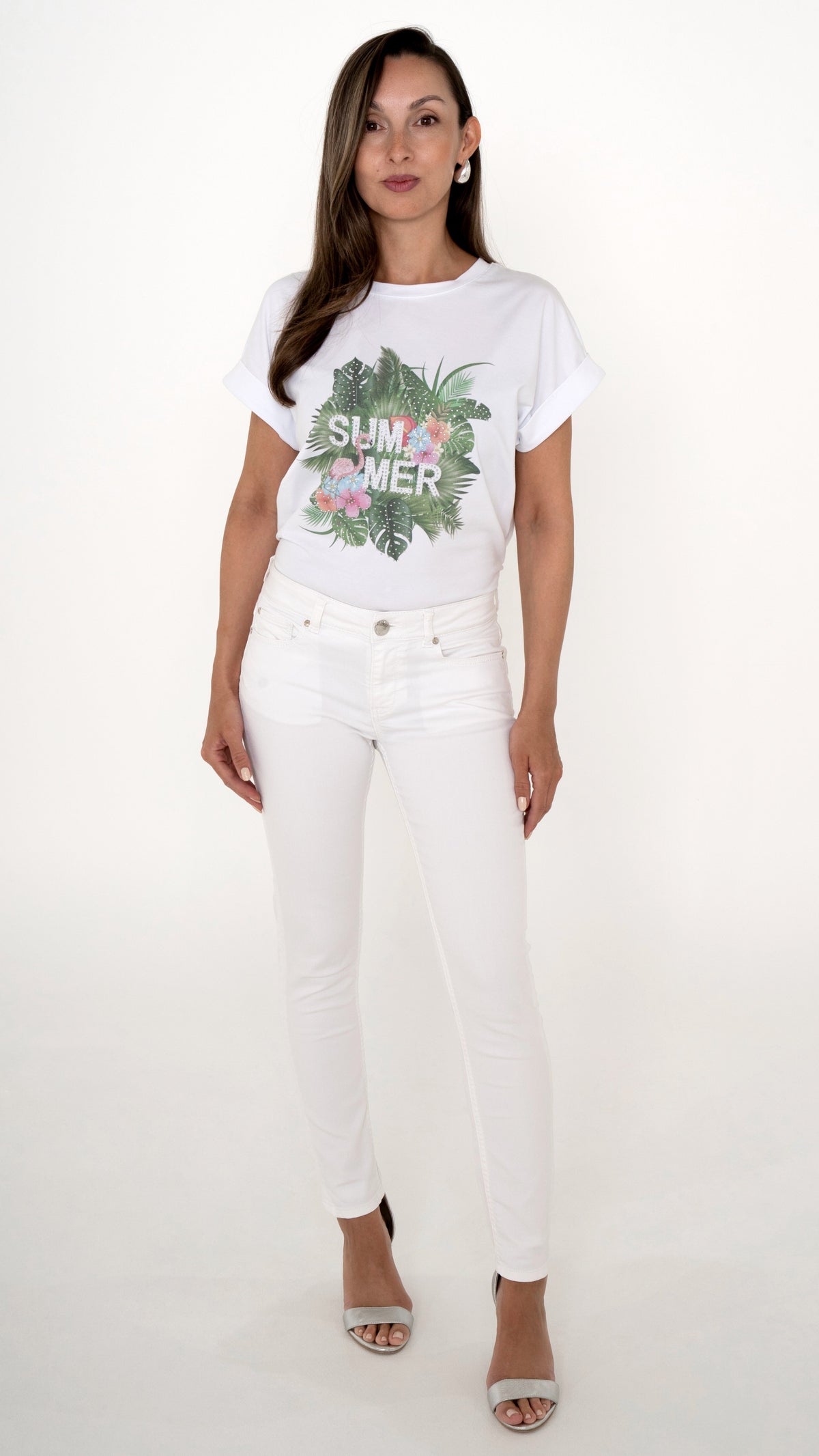 Feminine Sommer Damenmode in weiß: Model trägt ein weißes Outfit bestehend aus einer Skinny Denim Hose in weiß. Dazu ein weißes T-Shirt mit tropischem Sommer-Print mit Palmen und Blumen. Silberne Sandaletten