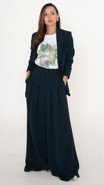 Feminine ausgefallene Damenmodein petrol: Model trägt ein modisdh Business Outfit bestehend aus einem Anzug in Petrol: langes Blazer und eine Hose mit Falten und ultra weitem Bein. Dazu ein weißes T-Shirt mit tropischem Sommer-Print mit Palmen und Blumen. Silberne Pumps