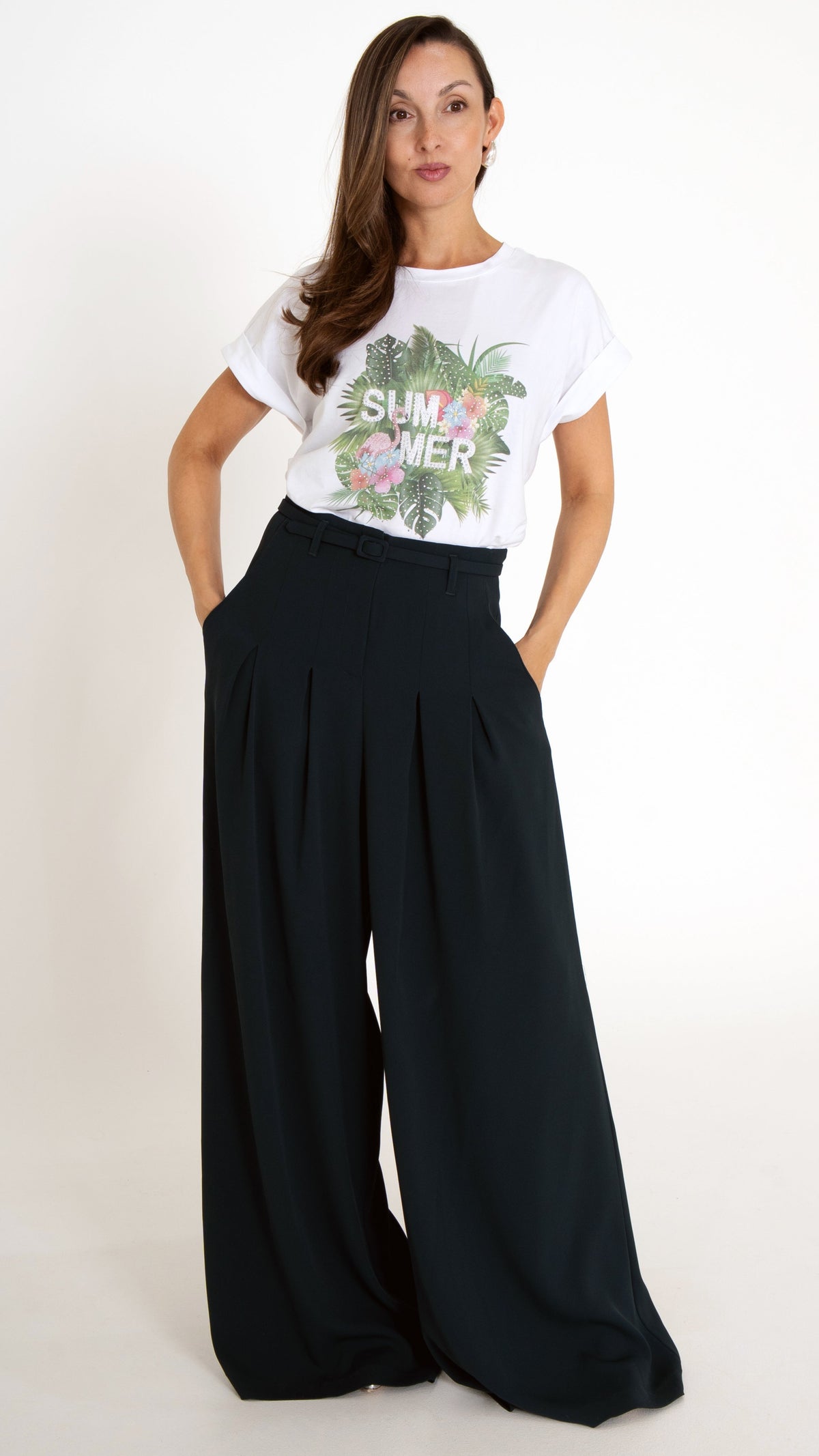 Feminine ausgefallene Damenmode: Model trägt ein weißes Sommer T-Shirt mit tropischem Palmendruck. Dazu trägt sie eine modische Stoffhose mit ultra weitem Bein in Petrol.