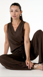 Fashion Editorial - Sitzende Ansicht: Model in sitzender Pose trägt ein sommerlich elegantes Outfit in der Farbe Mocca Braun: weite Leinenhose und passendes Top mit V-Ausschnittärmellos