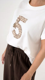 Detailansicht Stickerei auf einem T-Shirt: Feminine und ausgefallene Damenmode: Model trägt eine weite Leinenhose in Mocca Braun und ein modernes Oversize T-Shirt mit lockerer Passform und einer Stickerei in Form einer 5. mit Perlen