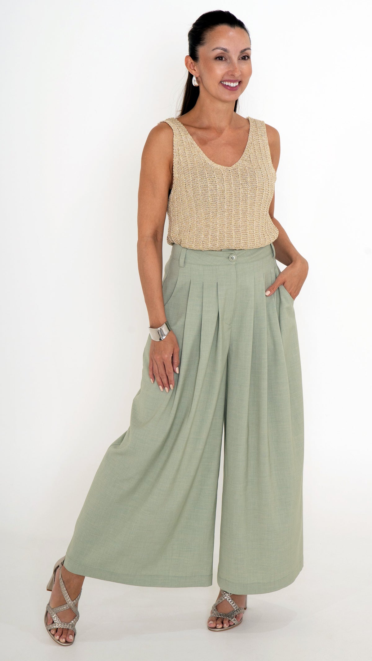 Elegante Damenbekleidung mit einem  ausgefallenen Sommeroutfit. Es besteht aus einer verkürzten Stoffhose mit Falten und extra weitem Bein in einem hellen Maigrün. Das Oberteil ist ein goldenes Stricktop mit leichtem Glanz, ohne Ärmel