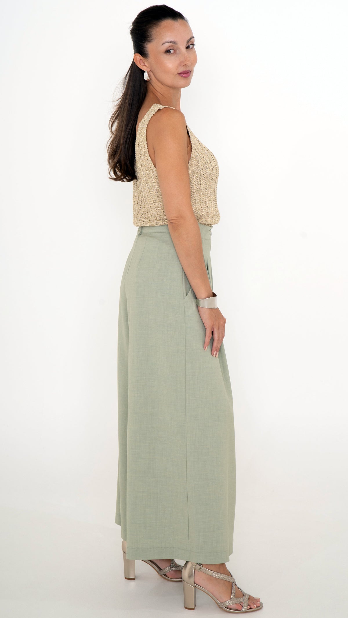 Seitenansicht eines Models mit femininer schicker Damenmode für den Sommer: Weite Stoffhose im Culotte Stil in der Farbe soft may green. Dazu trägt sie ein golodenes Stricktop