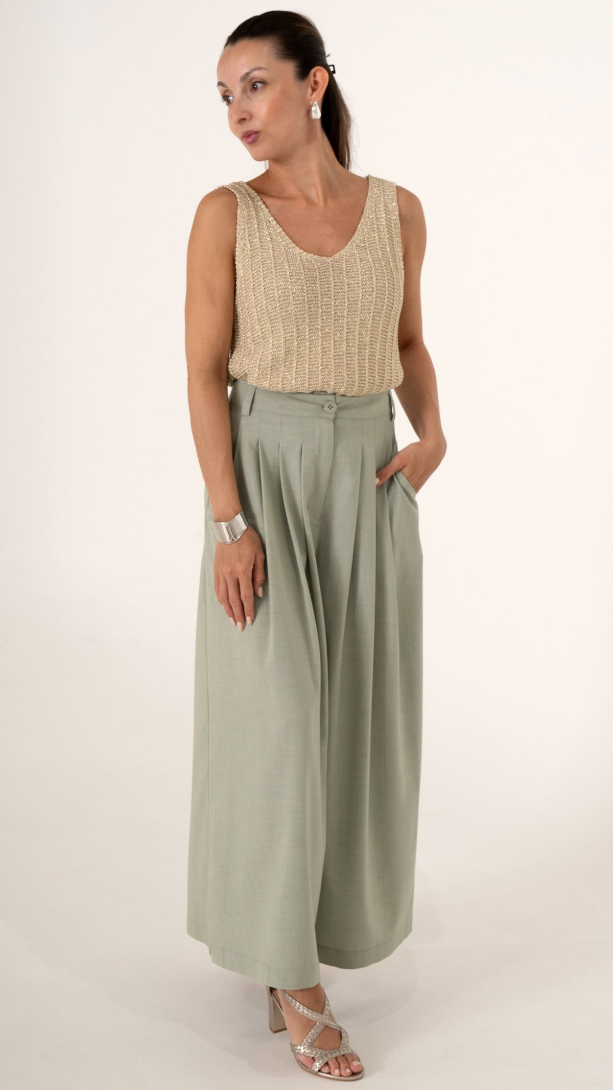Eine Frau trägt ein sommerlich feminines Outfit bestehend aus goldenem Stricktop ohne Ärmel und einer weiten verkürzten Faltenhose in soft may green
