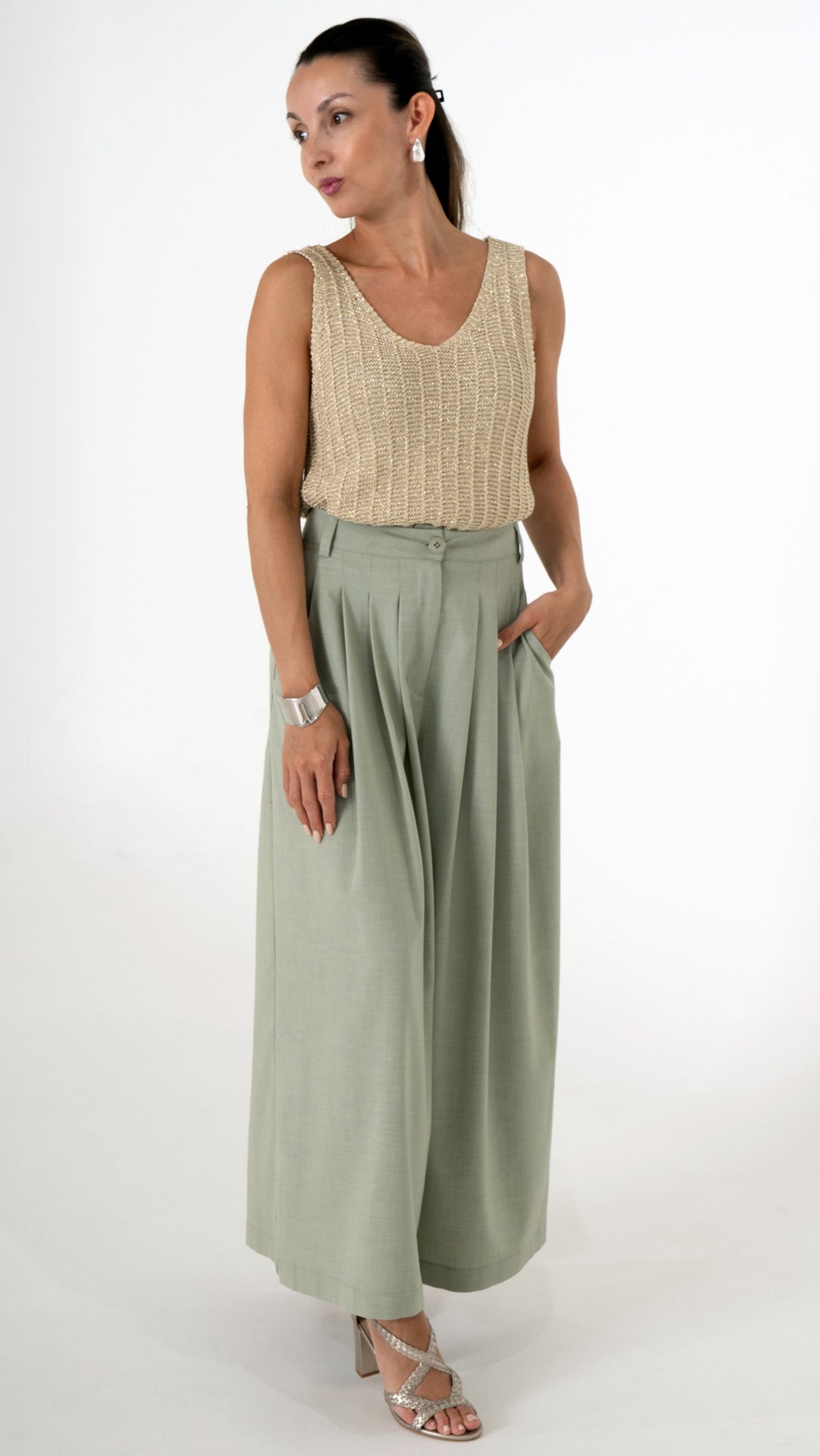 Elegante Damenbekleidung mit einem  stilvollen Sommeroutfit. Es besteht aus einer verkürzten Stoffhose mit Falten und extra weitem Bein in einem hellen Maigrün. Das Oberteil ist ein goldenes Stricktop mit leichtem Glanz, ohne Ärmel